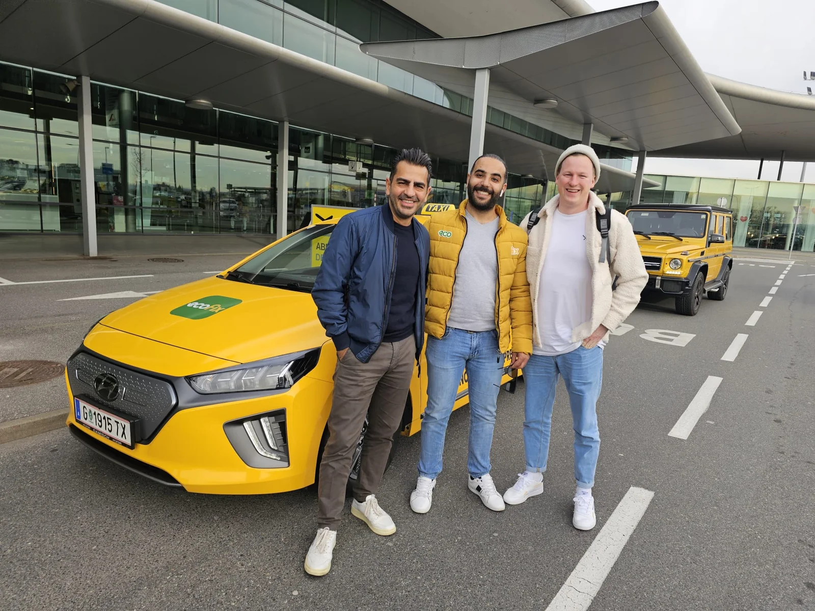 EcoFix Fahrer mit zwei Fahrgästen und einem E-Taxi am Flughafen Graz